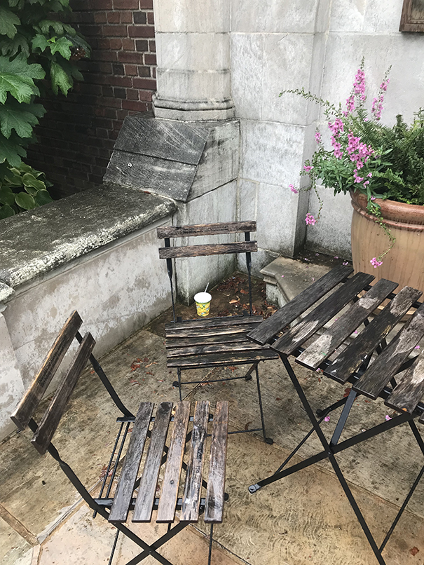 A small rustic table and chairs on a patio, and a Styrofoam cup beneath it all.